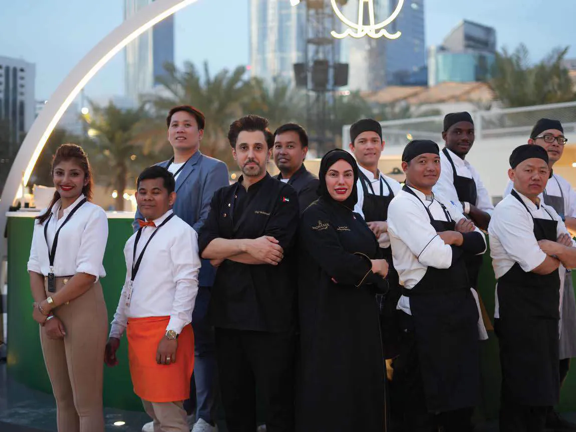 Chef Mariam Al Mansoori with her brigade at an outdoor event, the Abu Dhabi skyline behind